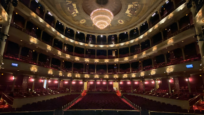 Interior of the Academy of Music, with red seats in four levels and a chandelier hanging from a gold-accented ceiling