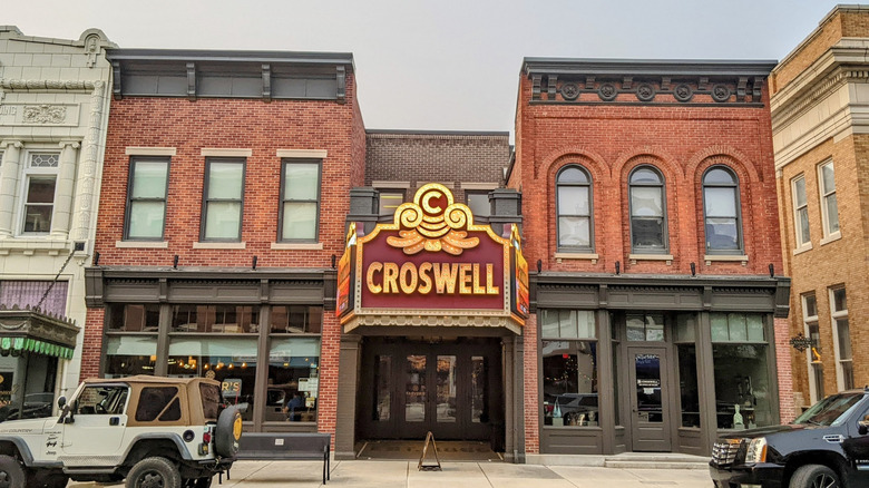 Croswell Opera House, a brick building with a yellow and red sign and gray accents, with a white jeep parked out front under a pale blue sky