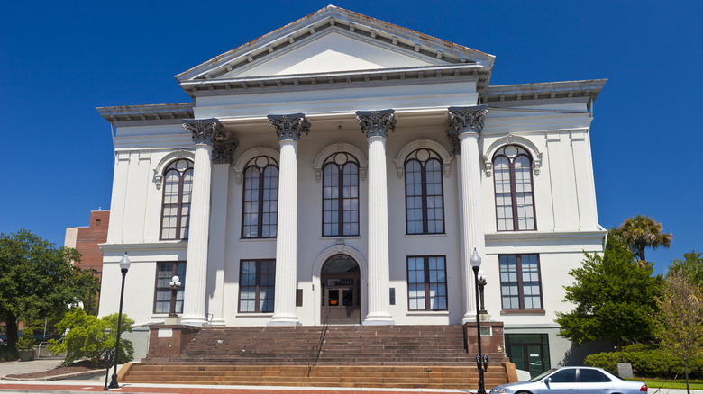 Thalian Hall, a white building with tall columns, arched windows, and brown steps, with trees to either side under a blue sky