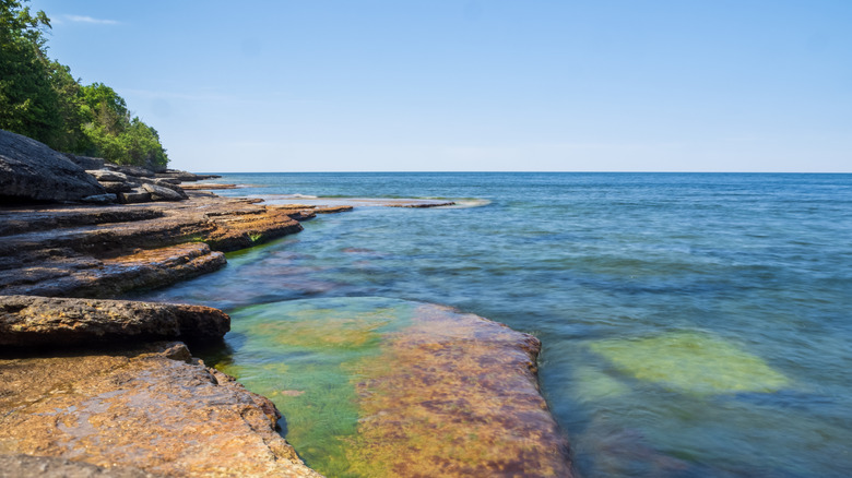 Sunlight dances on the clear water cascading over moss-covered cliffs by Lake Ontario at Robert G. Wehle State Park in Upstate New York