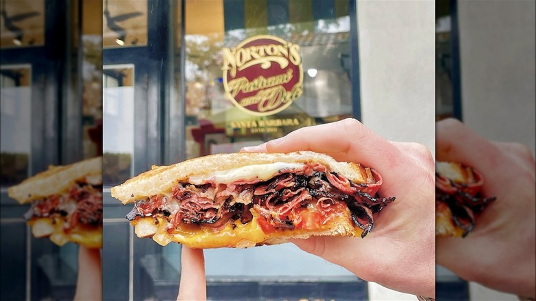hands holding up pastrami sandwich in front of Norton's