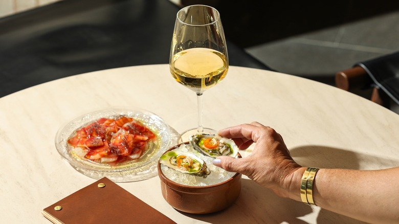 A hand reaching for oysters, surrounded by a glass of white wine and appetizers at Folia, Appellation Healdsburg's onsite restaurant