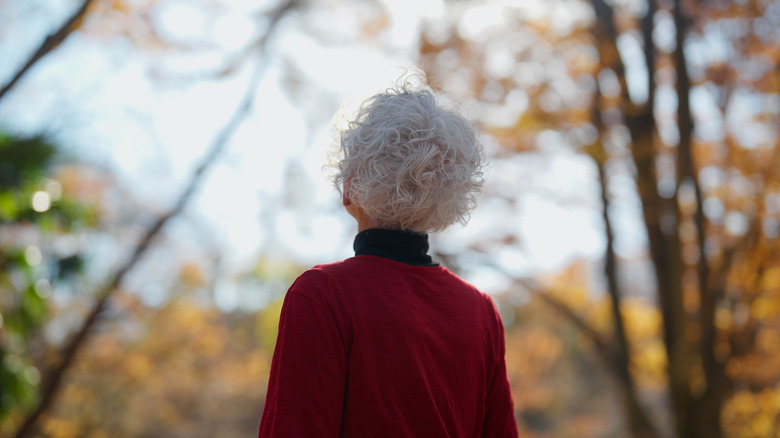 Woman in red sweater and grey hair looks at autumn trees