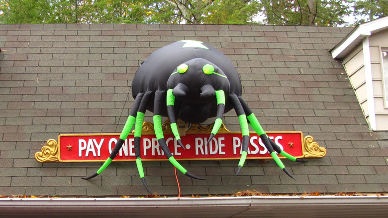 People wait in line to purchase tickets at an amusement park beneath a giant inflatable spider
