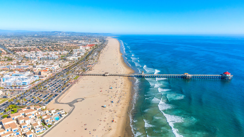 Aerial shot of Huntington Beach with its stretch of wide whit sand, deep blue water, low-rise buildings, and long pier.