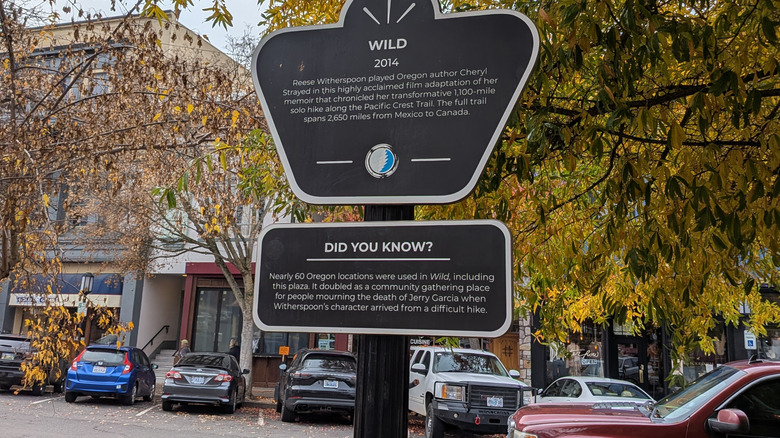 View of one of the many markers at a filming location for the movie "Wild" along the Oregon Film Trail, the first of its kind in the U.S., surrounded by colorful autumn trees and nearby vehicles in the town of Ashland's lively outdoor plaza area.