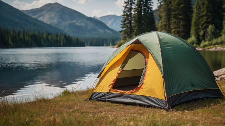 Yellow and green tent perched on the shore of a lake with mountains in the background