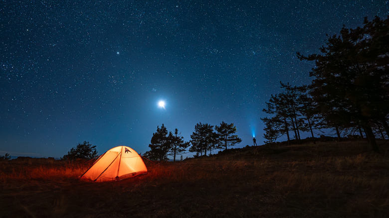Tent on a campground illuminated with a lamp on a starry night