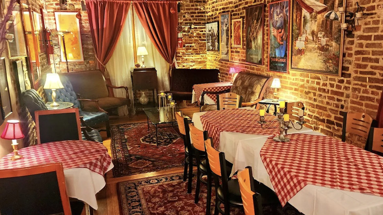 Interior view of Victor Cafe, Philadelphia, of a room with exposed brick walls, artwork, Persian-style rugs, and tables covered with red checked tablecloths with dim lighting