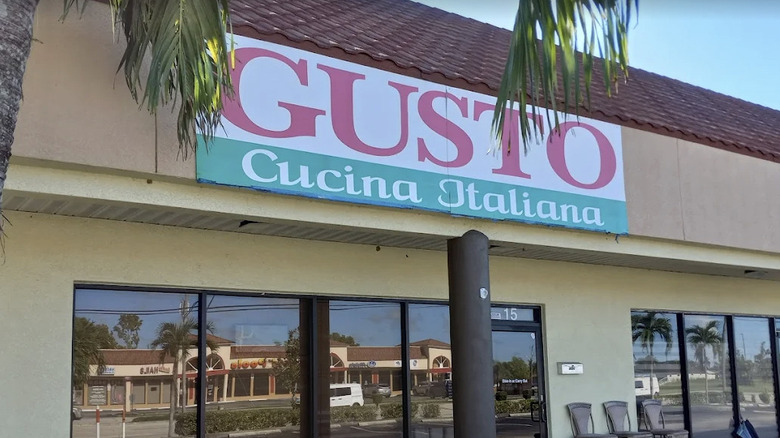 Exterior signage for Gusto Cucina Italiana on a Cape Coral strip mall with palm fronds hanging down in the daytime