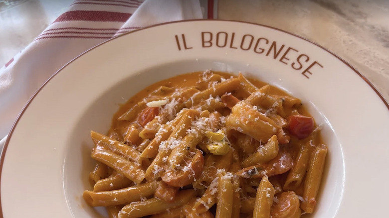 Close-up view of pasta in spicy vodka sauce on marble table in white dish with "Il Bolognese" in red, white and red striped napkin to the left