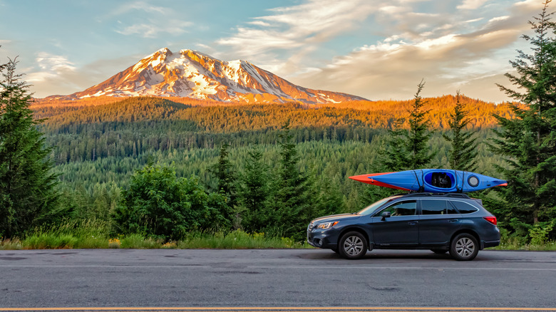 A car with kayaks on the roof is parked under a snow-capped mountain in Washington