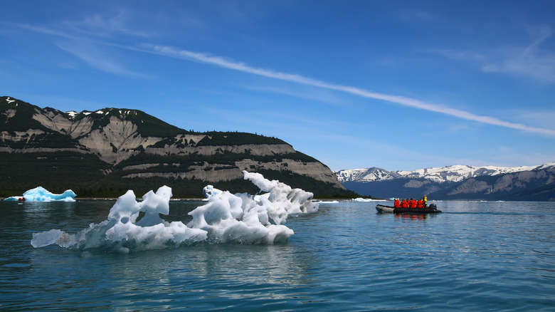 People in small boat in water near glacial ice