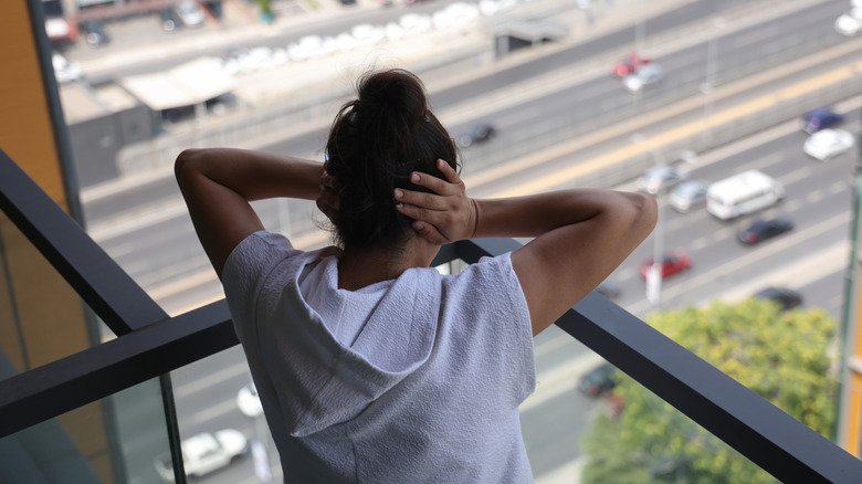 Woman seen from behind covering her ears on a balcony overlooking a city street