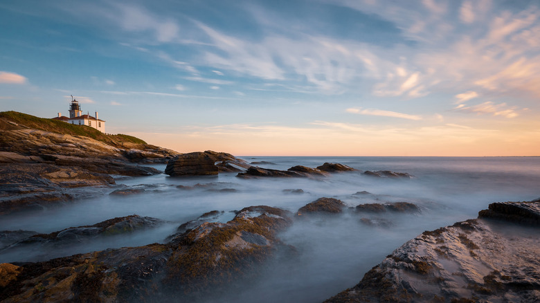 Beavertail lighthouse on rocky coastline over misty sea in Jamestown, Rhode Island