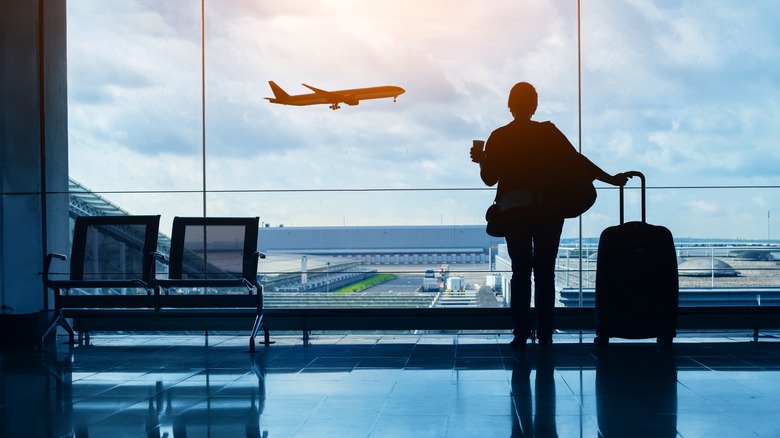 Woman at airport with luggage watching plane take off