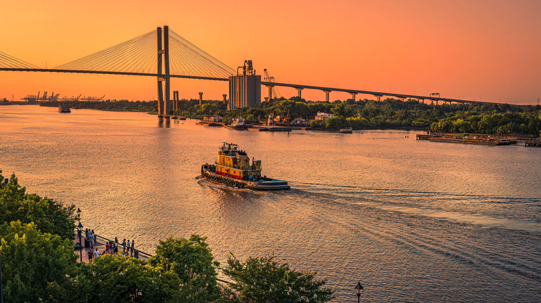 a boat makes its way out to see along the Savannah River in the evening, with orange skies illuminating the scene