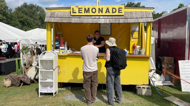 Two customers at a bright yellow lemonade stand at Brimfield Antique Flea Market, Massachusetts