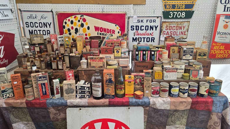 Vintage car signs above a table stacked with old bottles and cans at Brimfield Antique Flea Market, Massachusetts