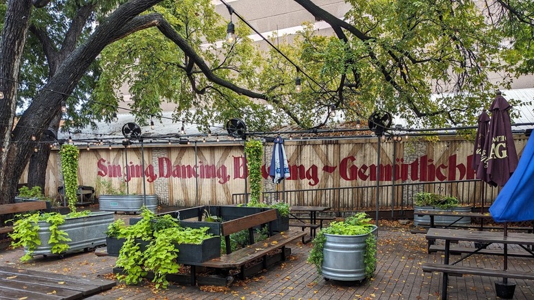 Scholz Garten exterior, showing writing in English and German along with greenery and picnic tables.