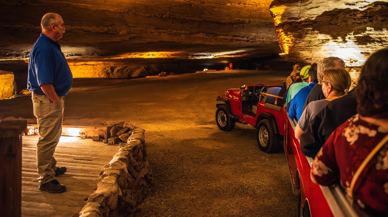 Guide standing in a lit-up underground cavern with people seated in jeep-pulled tram at Fantastic Caverns