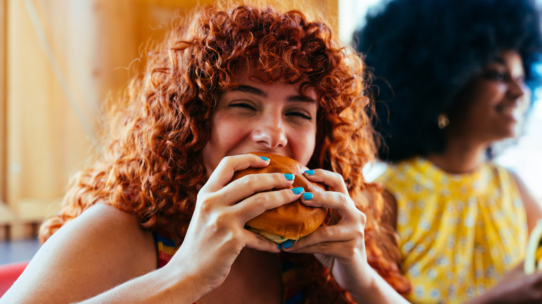 A happy woman bites into a burger
