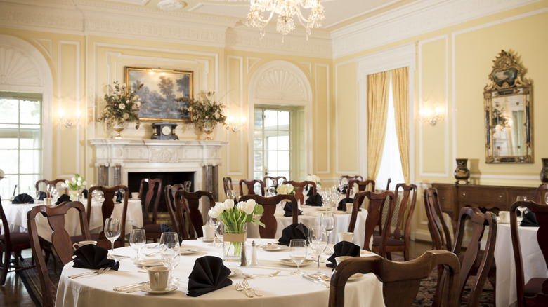 The yellow dining room at The Graylyn Estate with round tables set with white cloths, tulips, and wine glasses