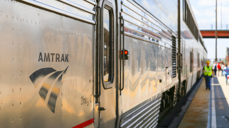 An Amtrak train in the station with a worker walking in the background