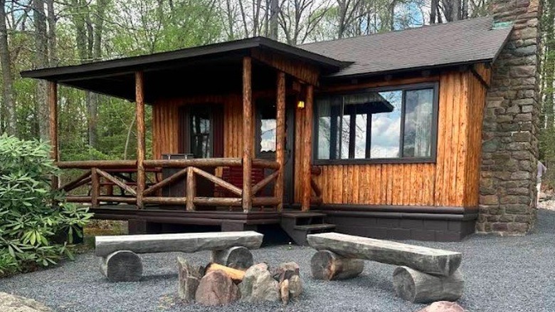 Exterior view of one of the wooden cabins, with an outdoor firepit and surrounded by forest, at Mountain Springs Lake Resort in the Poconos, Pennsylvania