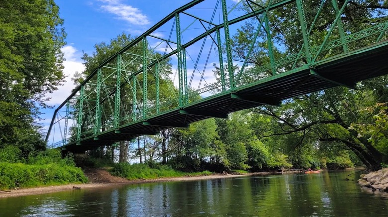 Views of a green bridge spanning over a scenic river, surrounded by lush greenery, in the town of Daelville, Indiana