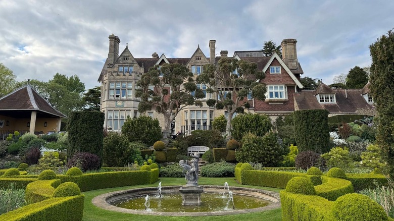Front view of Hambleton Hall in the town of Hambleton, UK with green lawns, a fountain and tall tudor structure behind