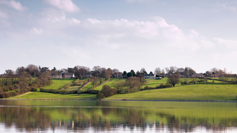 View of the village of Hambleton from Rutland Water, green rolling hillsides and mirror image of the village in the water