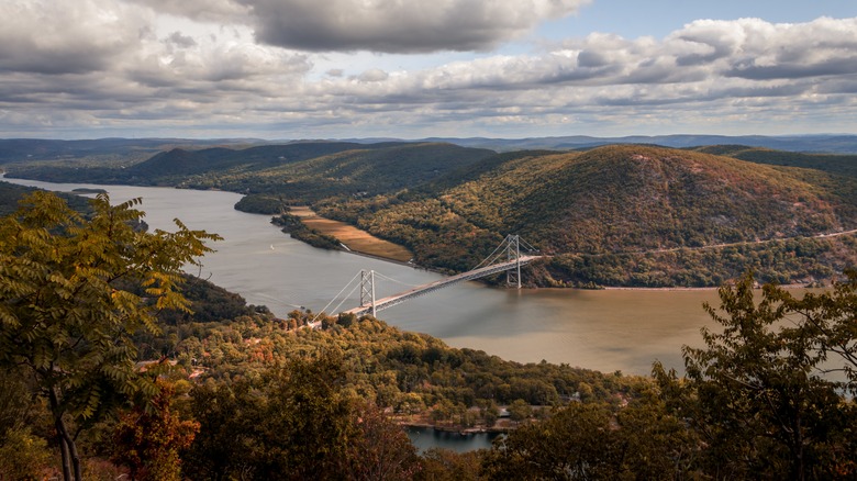 View of Bear Mountain State Park in New York during the day with a river and bridge shown in the distance.