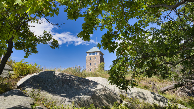 View of the Perkins Memorial Tower in Bear Mountain State Park during the day with trees and rocks in the foreground.