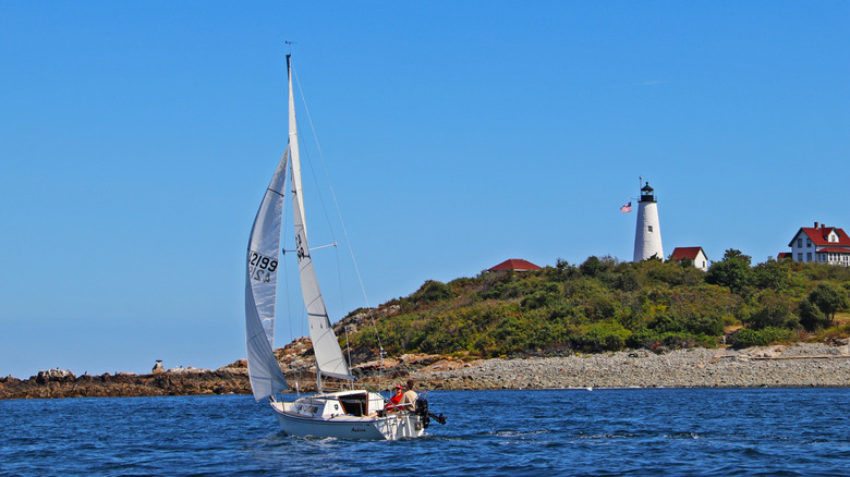 A sailboat is pictured off the coast of Bakers Island in Salem Sound, Massachusetts, with a lighthouse and the historic assistant keeper's house in the background.