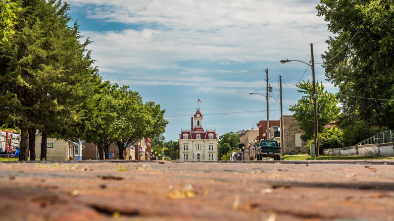 Road lined with trees, leading to white and red courthouse in Cottonwood Falls