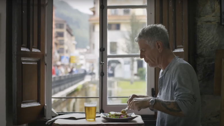 Profile shot of Anthony Bourdain eating with a glass of beer beside