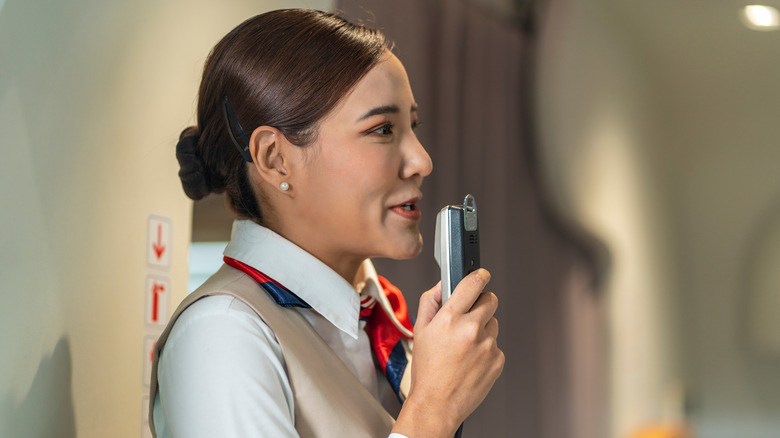 A female flight attendant speaking into the speaker making an announcement