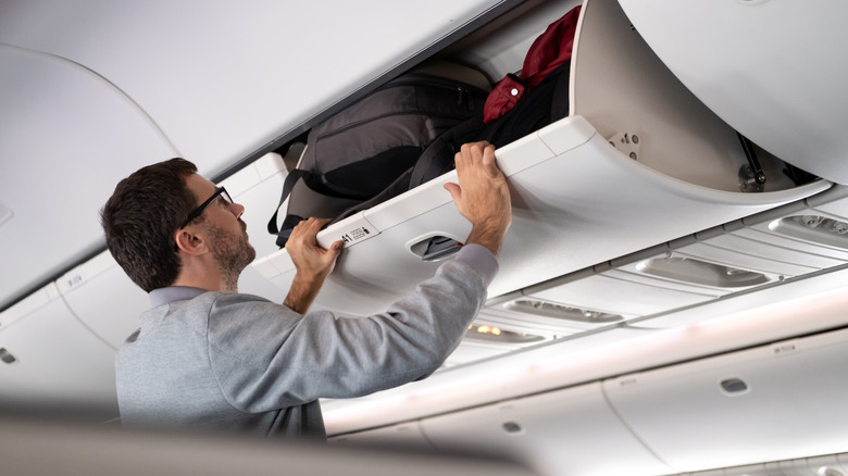 A man shuts the overhead compartment on an airplane