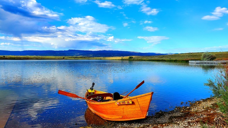 Empty orange boat on shore of Becker Lake with blue sky and mountains in background