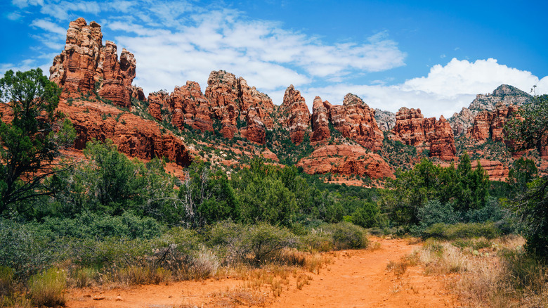 Red dirt trail leading into red rock formation with blue sky
