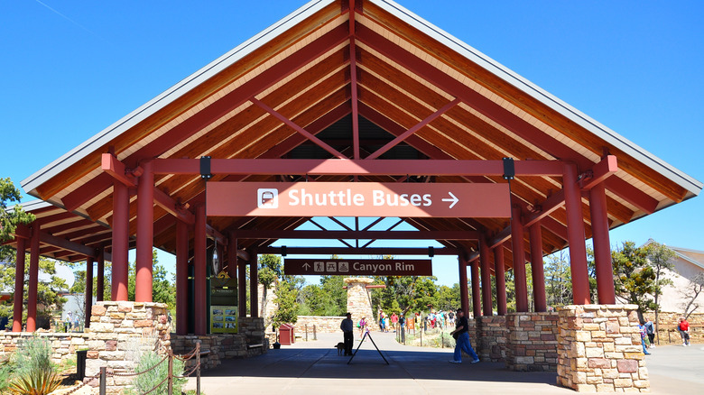 Visitors stand under a brown shuttle bus waiting pavilion at the Grand Canyon, near Tusayan