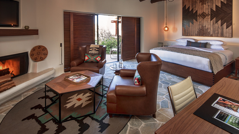 Interior view of one of the Casitas (guest suites) at Boulders Resort & Spa Scottsdale, a five-star luxury resort located in the town of Carefree in central Arizona, with a workspace, bed, sitting area, and fireplace visible in the foreground.