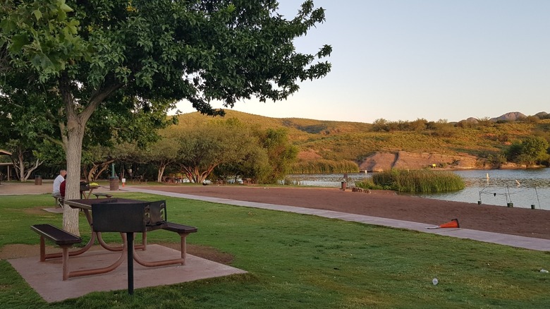 A picnic table and grill overlook the sandy beach and calm lake water at Patagonia Lake State Park in Arizona.