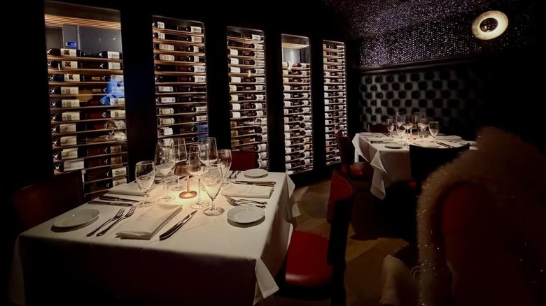 A dimly lit dining room with wine bottles and set tables in Durant's Steakhouse