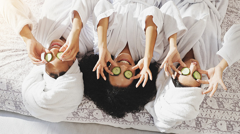 Women in a spa wearing white bathrobes and putting cucumber on their eyes
