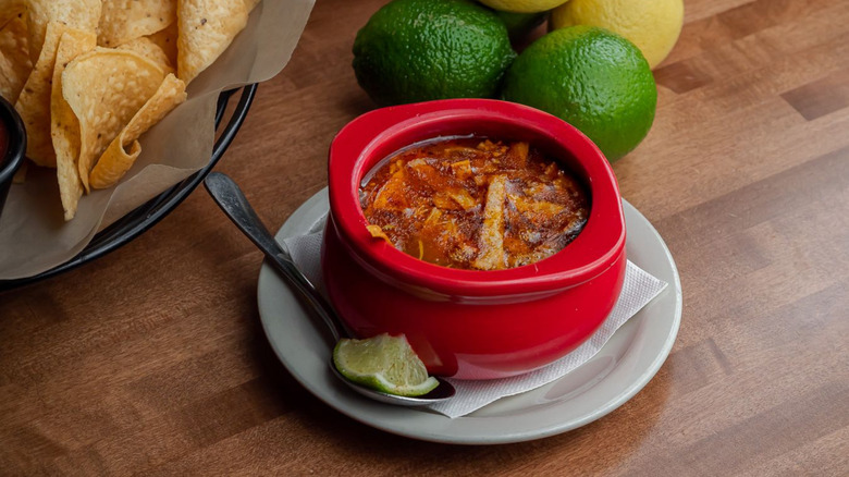 A hearty soup stands next to limes and chips at Cocina Madrigal in Phoenix, Arizona