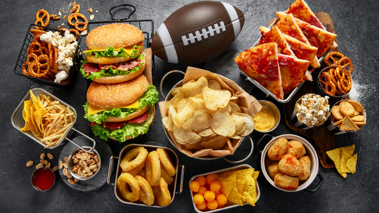 Game-day foods like pizza, burgers, fried foods, and snacks with a football
