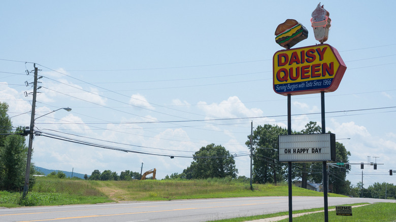 red and yellow sign next to power lines and an empty black road under blue sky