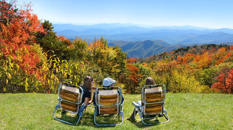 A family of three sitting in folding chairs and looking out at fall foliage covering the Blue Ridge Mountains around Asheville, North Carolina